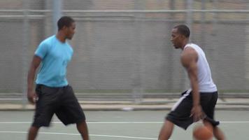 twee jonge mannen spelen één op één basketbal tegen elkaar.