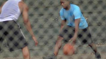 Dos jóvenes jugadores de baloncesto jugando uno a uno en una cancha al aire libre.