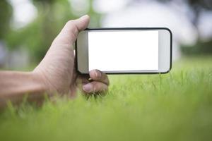 Cerrar la mano del hombre con el teléfono inteligente en el parque verde, maqueta de la pantalla en blanco del teléfono inteligente foto