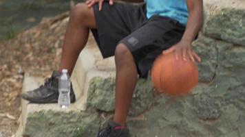 Retrato de un joven jugador de baloncesto regateando una pelota de baloncesto mientras está sentado.