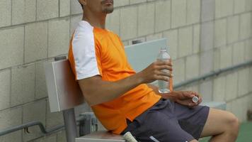 tenista bebiendo agua mientras descansa en un banco. video