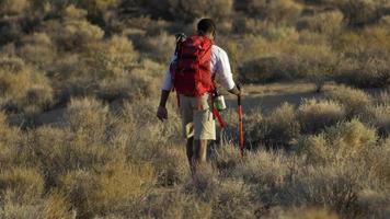 um jovem mochilando em um deserto montanhoso.