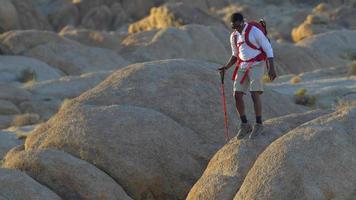 un giovane zaino in spalla su massi in un deserto montuoso. video