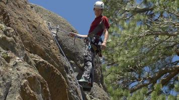 un joven que se repele por una montaña mientras escala en roca. video