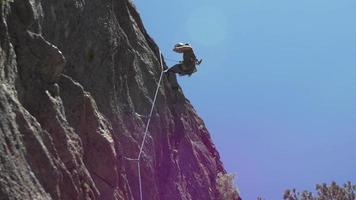un joven que se repele por una montaña mientras escala en roca. video