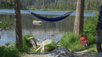 un hombre descansando en una hamaca cerca de un lago de montaña. video