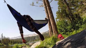 un uomo che riposa su un'amaca vicino a un lago di montagna. video