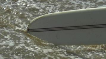 un homme marchant avec sa planche de surf longboard à la plage.