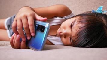 schattig klein meisje liggend op de bank in de woonkamer, camera kijken en glimlachen tijdens het spelen thuis. video