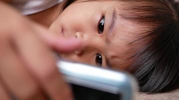 Cute little girl lying on the sofa and watching a smartphone in the living room. video