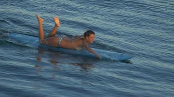 una mujer joven que practica surf en bikini en una tabla de surf longboard. video