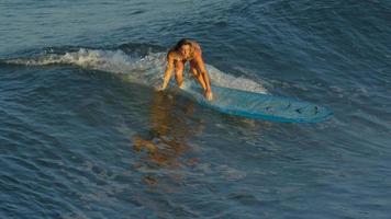 una mujer joven que practica surf en bikini en una tabla de surf longboard. video