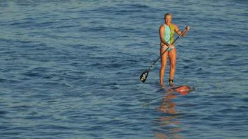 een jonge vrouw sup surfen in een bikini op een stand-up paddleboard surfplank. video