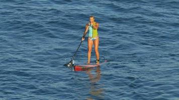 une jeune femme surf en bikini sur une planche de surf stand-up paddleboard. video