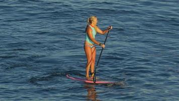 una giovane donna che fa surf in bikini su una tavola da surf stand-up paddleboard.