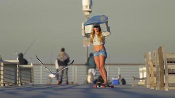 een jonge vrouw longboard skateboarden terwijl ze een surfplank op haar hoofd balanceert.