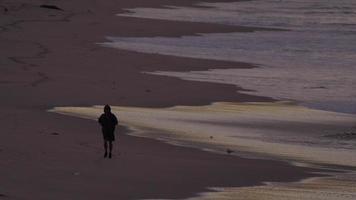 A man jogging on the beach at dawn.