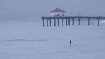 ein mann stand-up-paddleboards in der nähe des manhattan beach piers.