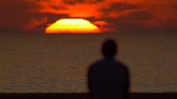 silhouet van een man die naar de zonsondergang op het strand kijkt. video