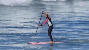 una donna cavalca un sup stand up paddleboard mentre naviga su una tavola da surf rosa.