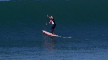 uma mulher monta uma prancha sup stand up enquanto surfa em uma prancha rosa.