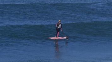 una donna cavalca un sup stand up paddleboard mentre naviga su una tavola da surf rosa.