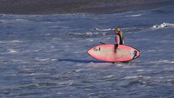 une femme fait du sup stand up paddle en surfant sur une planche de surf rose.