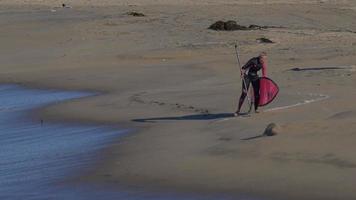 une femme fait du sup stand up paddle en surfant sur une planche de surf rose.