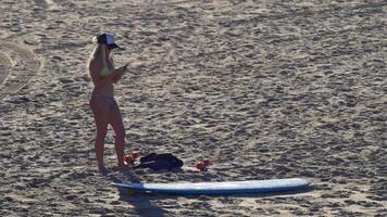 une jeune femme envoyant des SMS sur son appareil mobile une planche de surf longboard. video