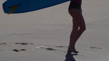 une jeune femme marchant avec sa planche de surf longboard.
