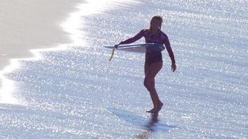 une jeune femme marchant avec sa planche de surf longboard.