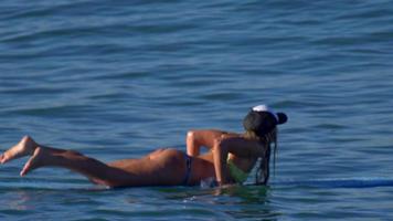 une jeune femme en bikini pagayer sur une planche de surf longboard.