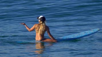 une jeune femme en bikini assise sur sa planche de surf longboard. video