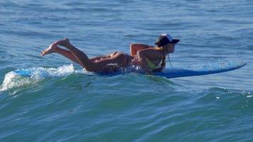 une jeune femme en bikini pagayer sur une planche de surf longboard.