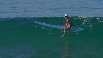 uma jovem de biquíni sentada em sua prancha de surf longboard. video