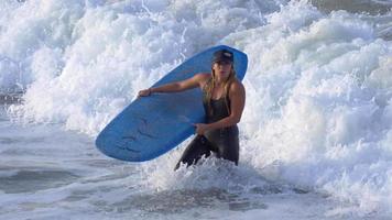 uma jovem com uma roupa de mergulho caminhando com sua prancha de surf longboard. video
