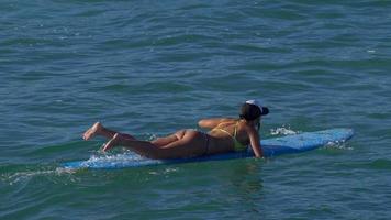 una giovane donna in bikini che rema su una tavola da surf longboard.