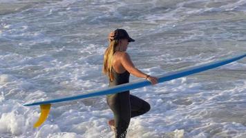 une jeune femme en combinaison de plongée marchant avec sa planche de surf longboard.