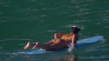 una giovane donna in bikini che rema su una tavola da surf longboard.