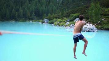 um homem tenta se equilibrar enquanto pratica slackline em uma corda bamba e caminha sobre um lago.
