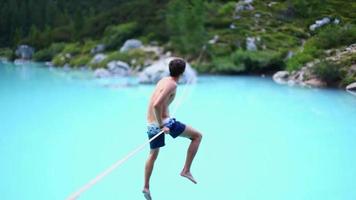 A man tries to balance while slacklining on a tightrope and walking over a lake. video