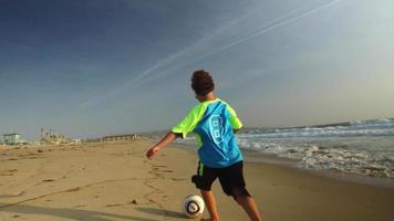 Ein Junge tritt bei Sonnenuntergang einen Fußball am Strand.