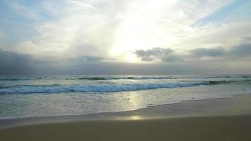 tracking shot van de golven van de oceaan, het strand en de pier bij zonsondergang.