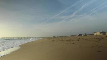 tracking shot van de golven van de oceaan, het strand en de pier bij zonsondergang.