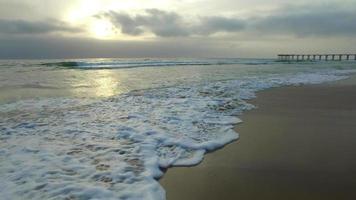 carrellata delle onde dell'oceano, spiaggia e molo al tramonto.
