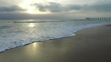 carrellata delle onde dell'oceano, spiaggia e molo al tramonto.