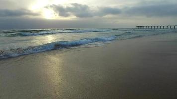 travelling des vagues de l'océan, de la plage et de la jetée au coucher du soleil.