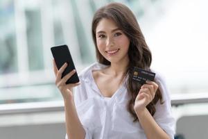 concepto de viernes negro, mujer sosteniendo el teléfono con tarjeta de crédito y sonriendo cerca de la tienda foto
