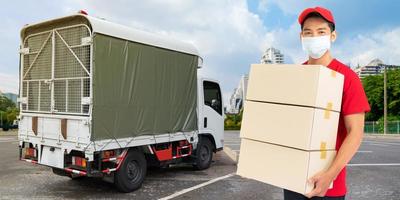 Delivery man employee in red t-shirt uniform face mask holding empty cardboard box photo