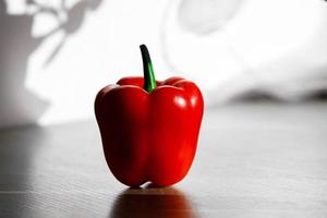 Pimiento rojo fresco sobre una mesa con luz solar desde la ventana de la cocina foto